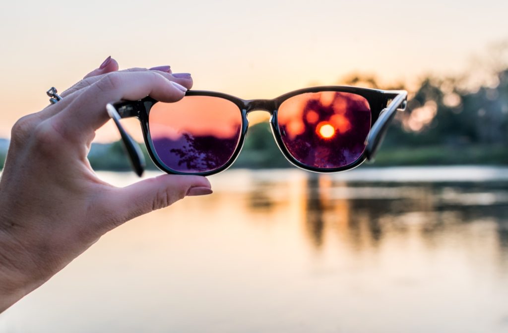 A person holding up a pair of polarized sunglasses in front of them